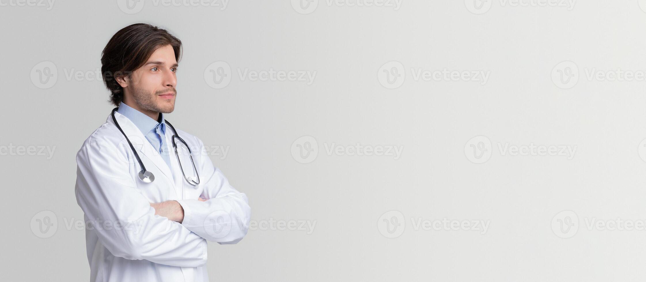 Portrait Of Thoughtful Male Doctor Standing With Folded Arms And Looking Away At Copy Space On Light Background, Panorama photo