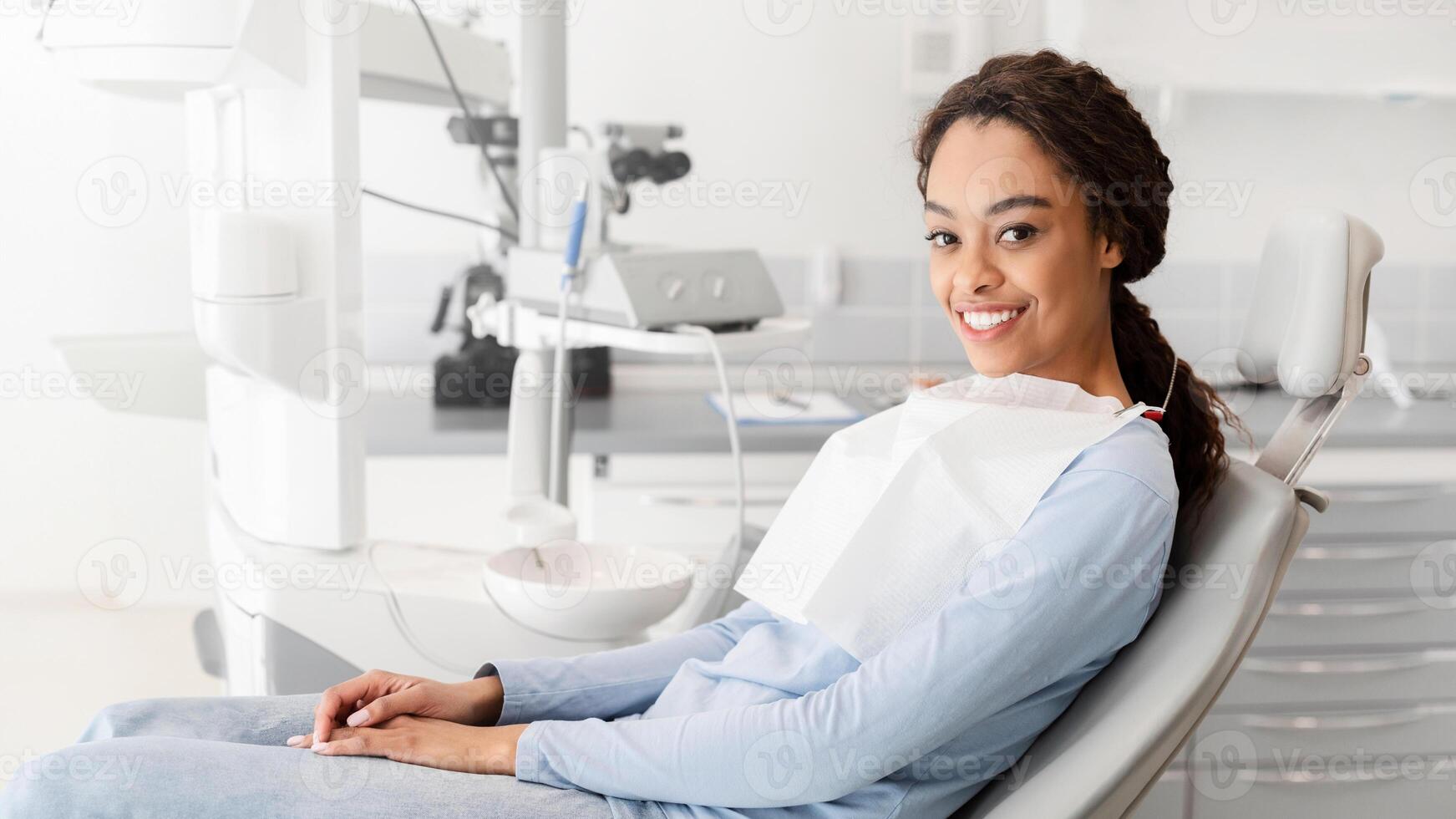 Young black lady sitting in dentist chair and smiling at camera, copy space photo