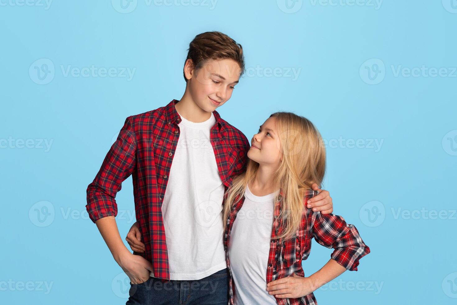 Siblings Love. Portrait of happy preteen brother and sister embracing and looking at each other, posing over blue background in studio, copy space photo