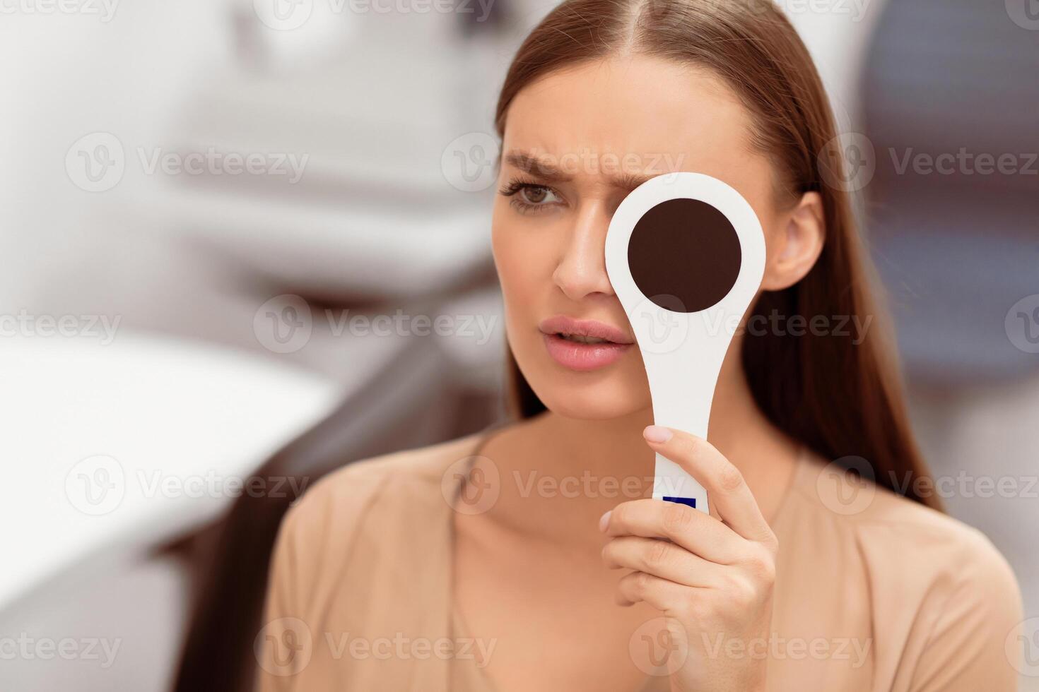 Poor Vision Concept. Close up portrait of anxious woman reviewing eyesight closing eye with occluder, looking at test chart photo