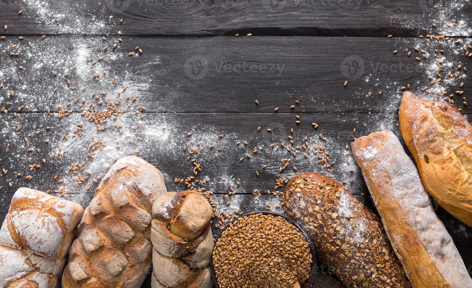 Bread border on dark wood with copy space background. Brown and white whole grain loaves still life composition with wheat flour sprinkled around. Bakery, cooking and grocery store concept. photo