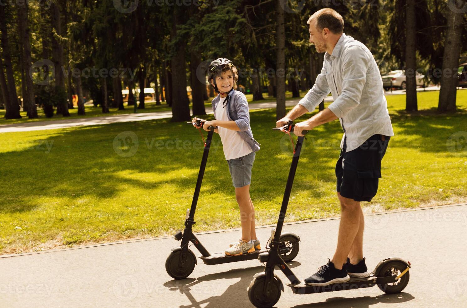 Bonding Concept. Father having ride on e-scooter with his cheerful son on the road in park, free space photo