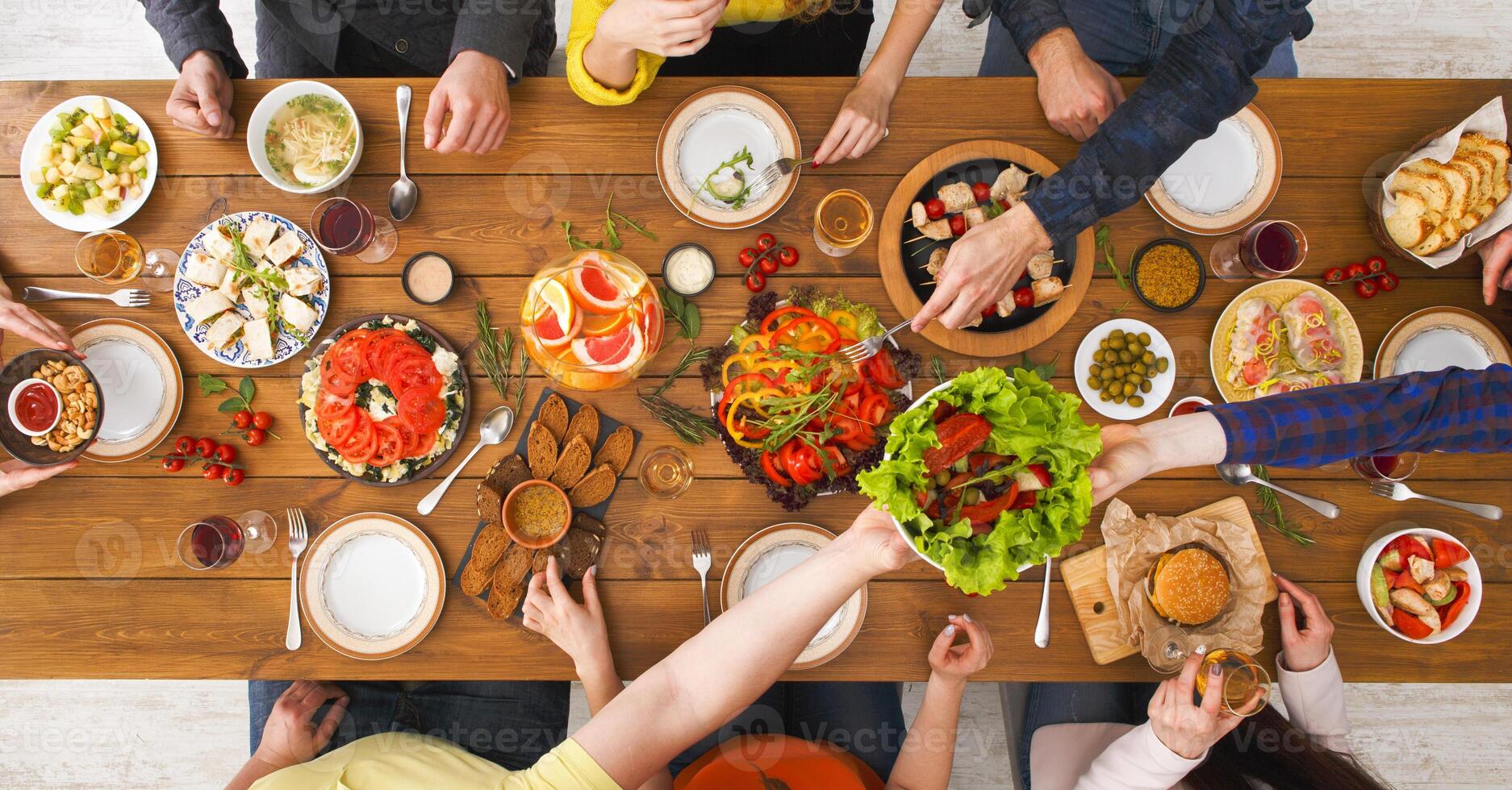 People eat healthy meals at festive table served for party. Friends celebrate with organic food on wooden table top view. Happy company having lunch, taking salad dish photo