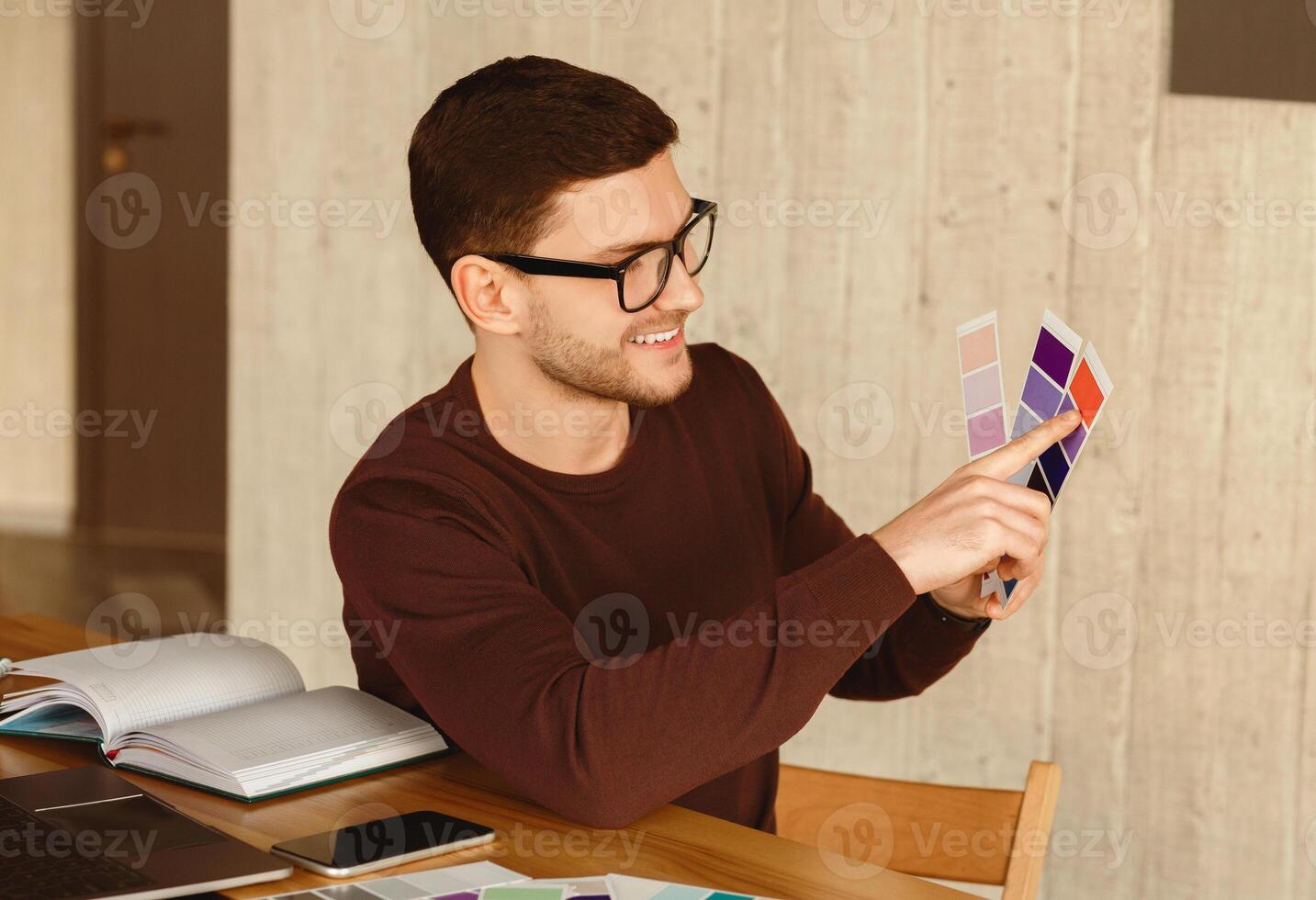 Designer Guy Choosing Color Samples For His Project Sitting At Workplace In Modern Office. Selective Focus photo