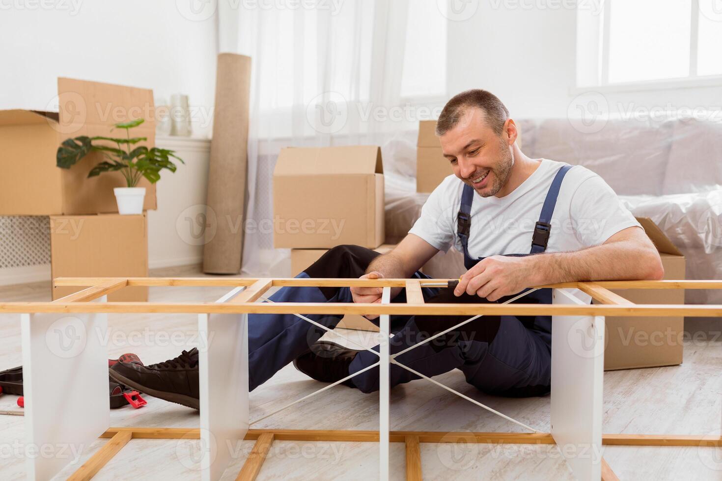 Happy Furniture Assembler In Blue Coverall Fixing Shelf With Screwdriver Providing Assembling And Transportation Services Working Indoor photo