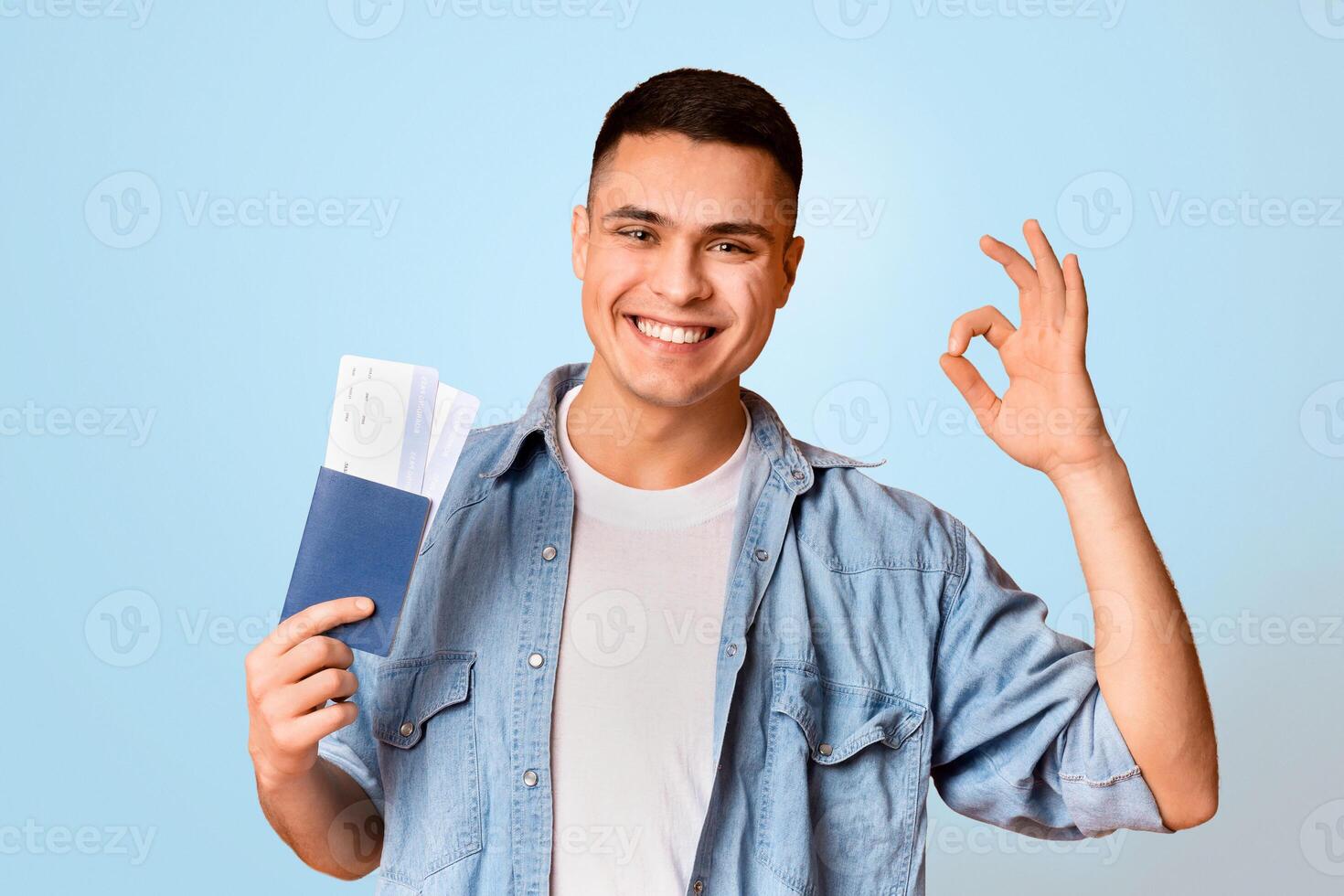Happy young man with passport and flight tickets showing okay gesture over orange background photo