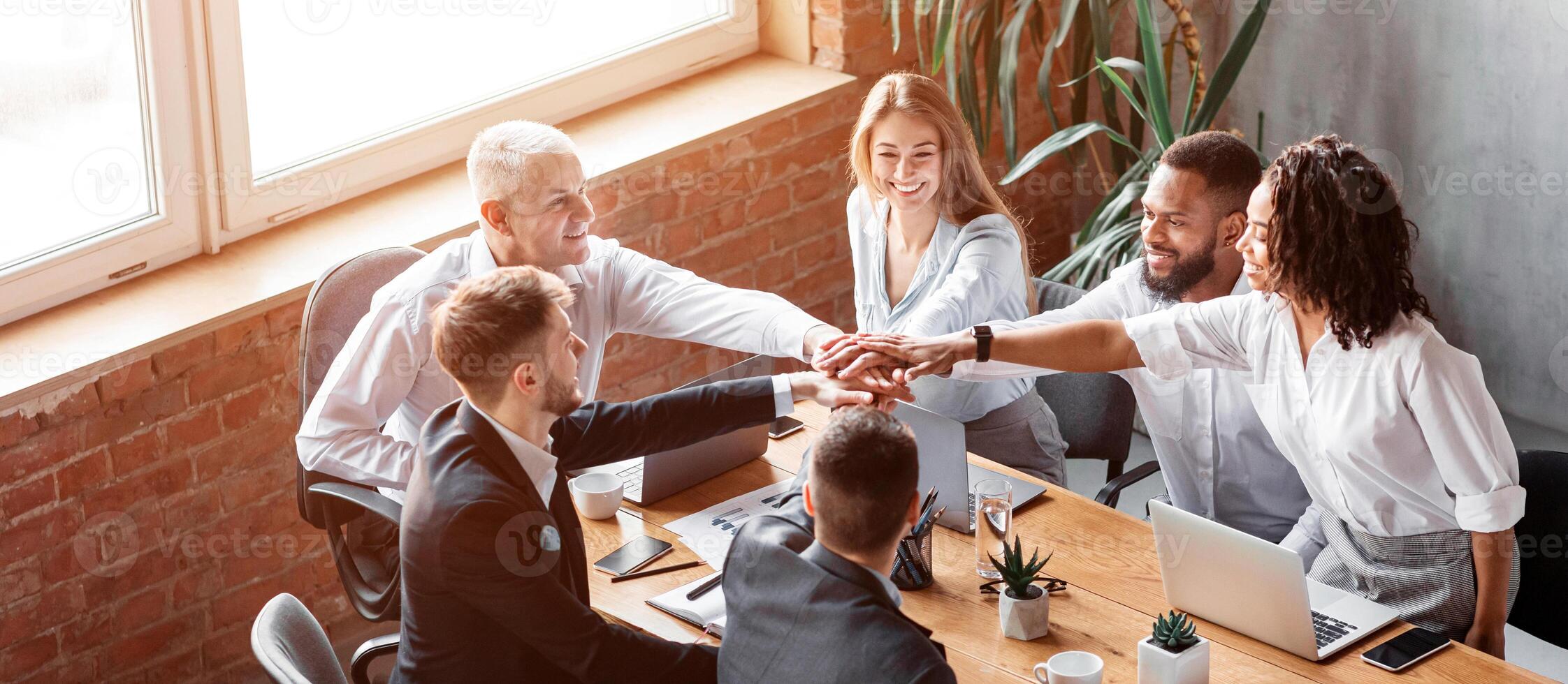 Teamwork And Unity. Business Colleagues Holding Hands During Corporate Teambuilding Meeting Sitting Together At Desk In Modern Office. photo