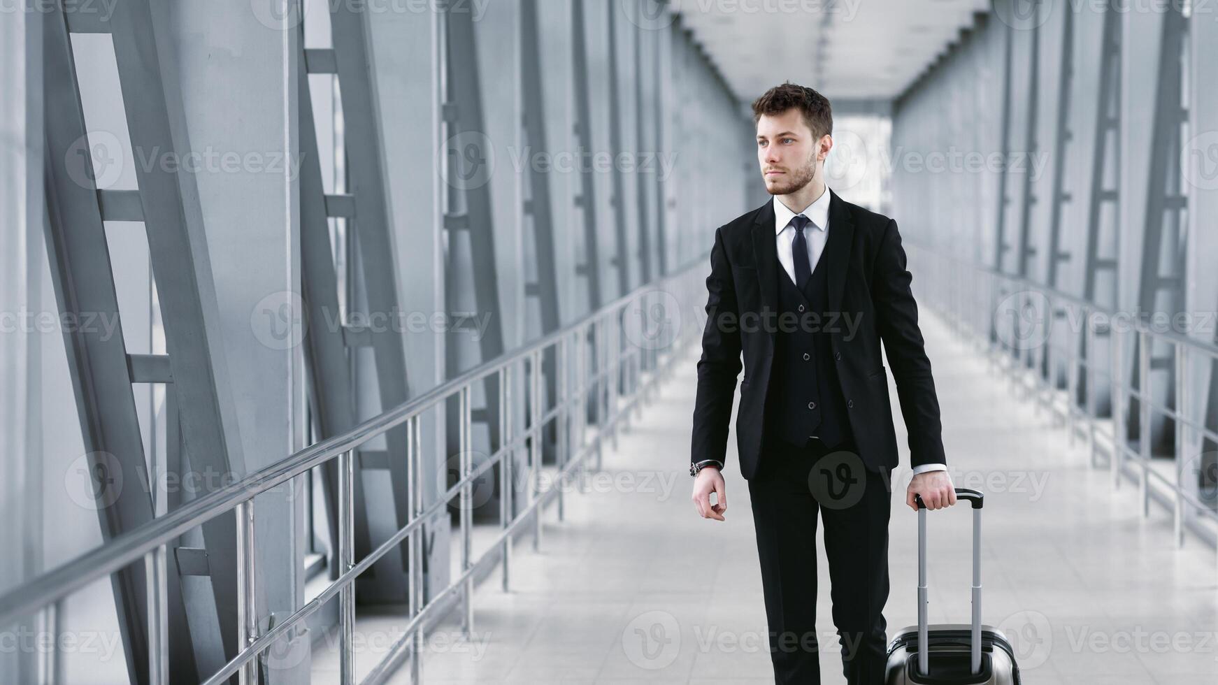 Travelling Businessman. Front view of bearded guy in formal wear pulling trolley bag walking in the airport, copy space photo