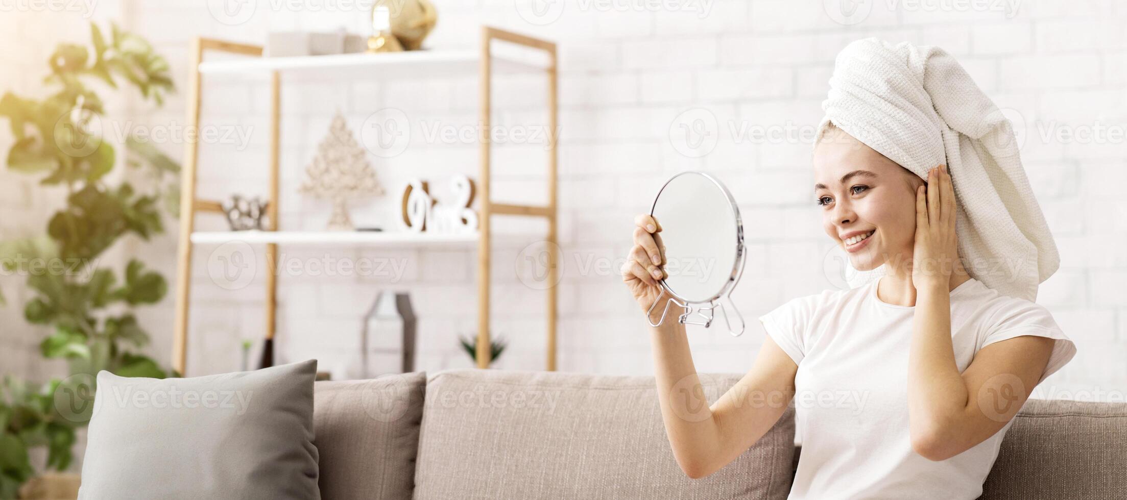 Face care concept. Young pretty woman looking at mirror, wearing towel on head after shower, free space photo