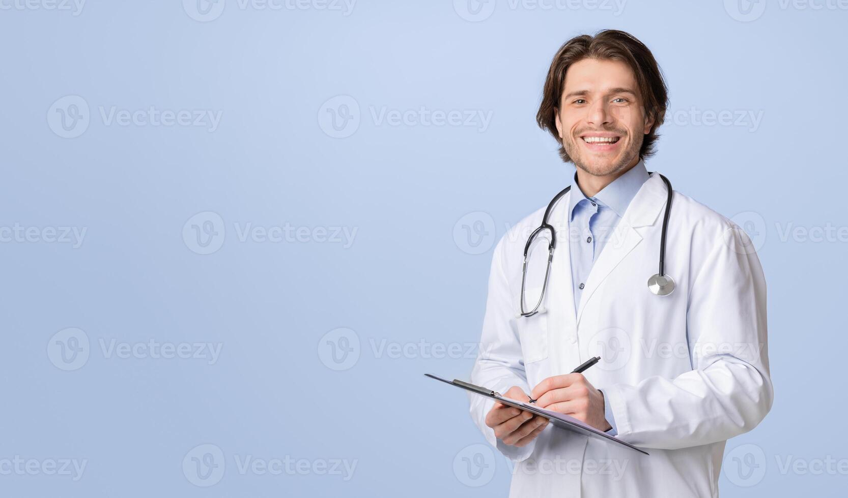 Health Insurance. Portrait Of Young Friendly Doctor With Medical Chart In Hands Posing Over Light Studio Background, Smiling At Camera, Copy Space photo