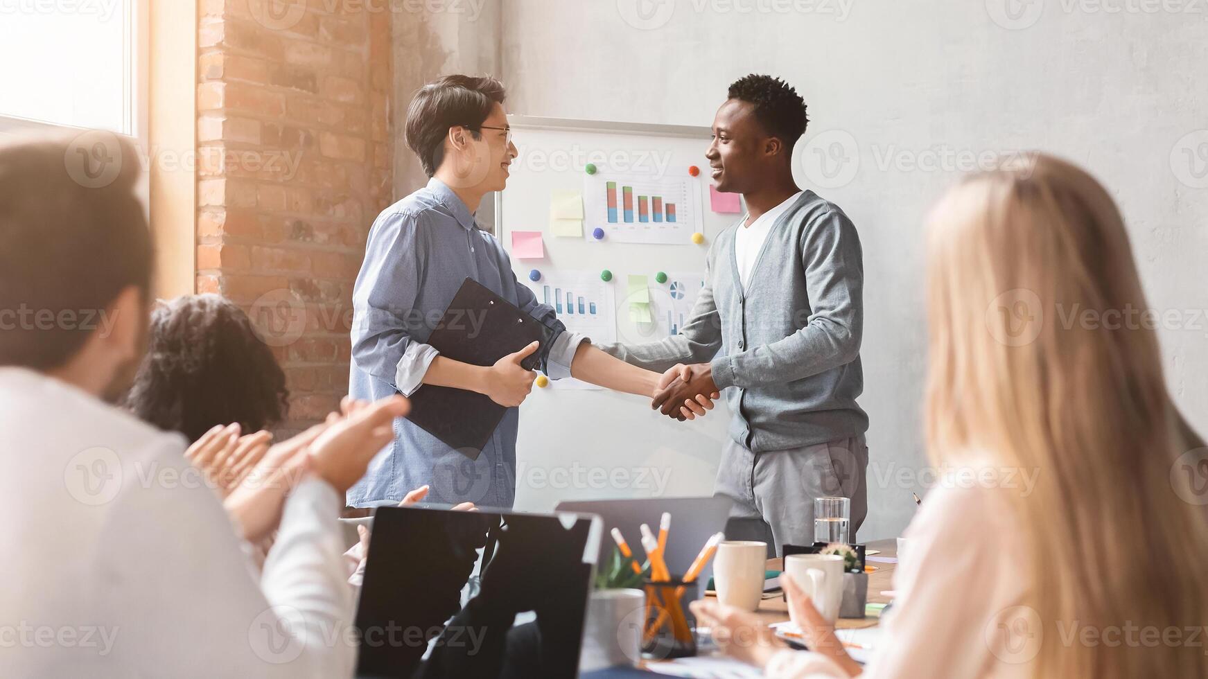 Young black manager shaking hand to asian employee after successful speech on morning briefing in office, international colleagues apllausing photo
