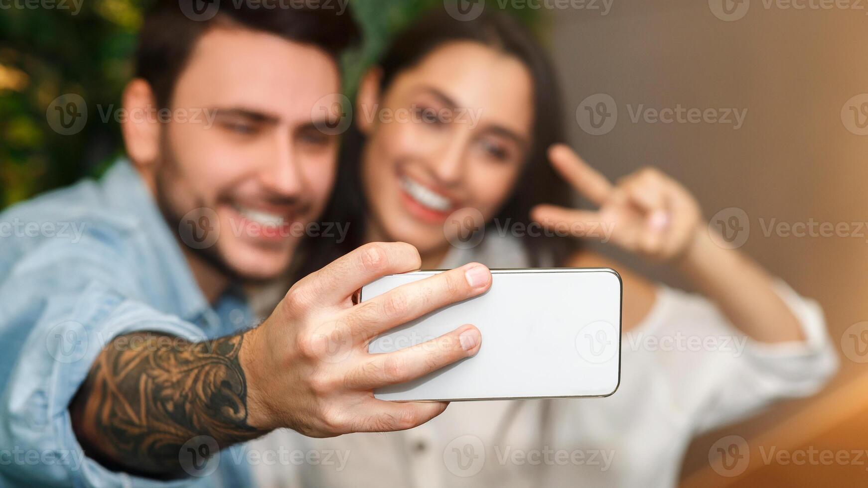 Happy Couple Making Selfie On Smartphone Gesturing V-Sign Having Fun During Romantic Date Sitting Together In Cafe. Selective Focus photo