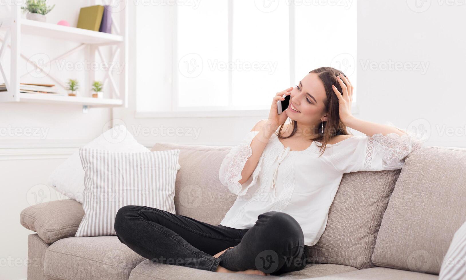 Happy woman talking on mobile phone sitting on comfortable couch at home, copy space photo