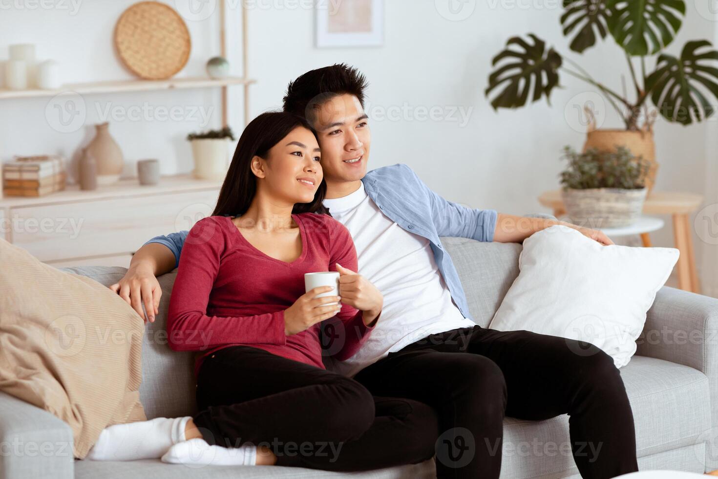 Smiling asian couple relaxing and watching TV at home, having rest after hard moving day, copy space photo