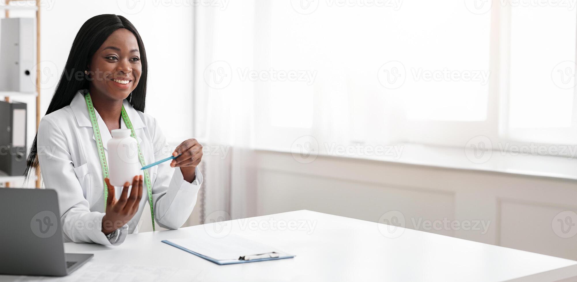 Smiling black dietologist explaining patient how to use pills, empty space photo
