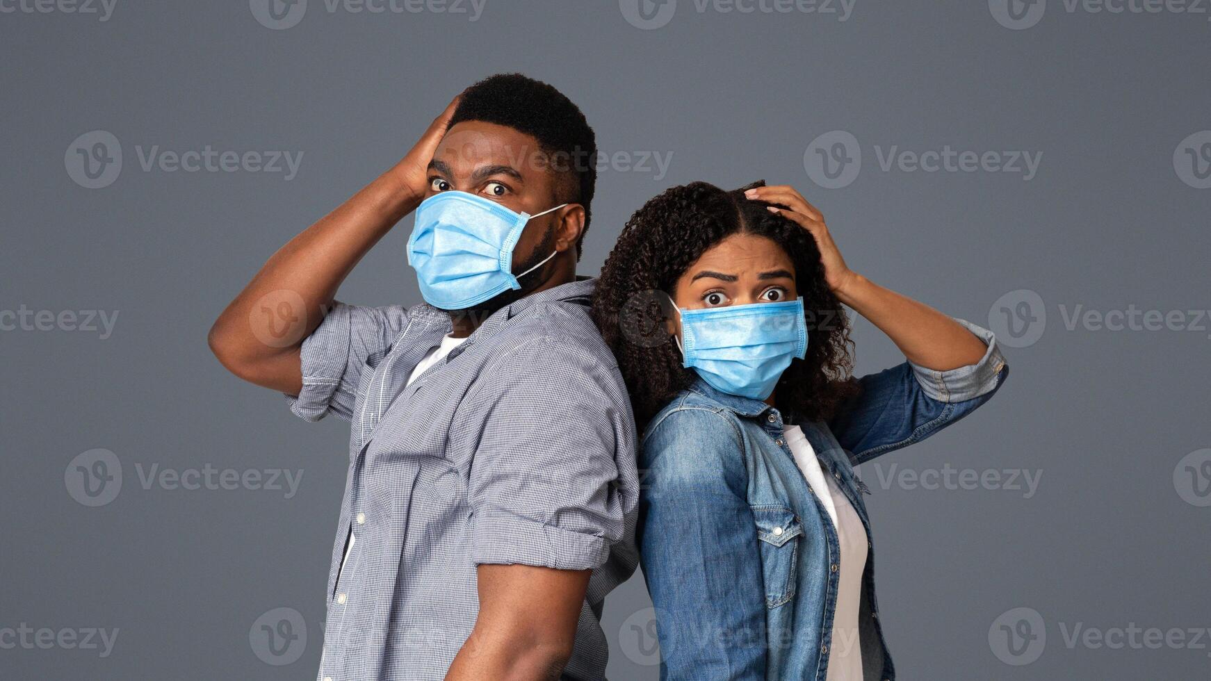 Afraid African American Couple Wearing Protective Face Masks And Holding Head With Hand, Panicking About Epidemy Over Light Background photo