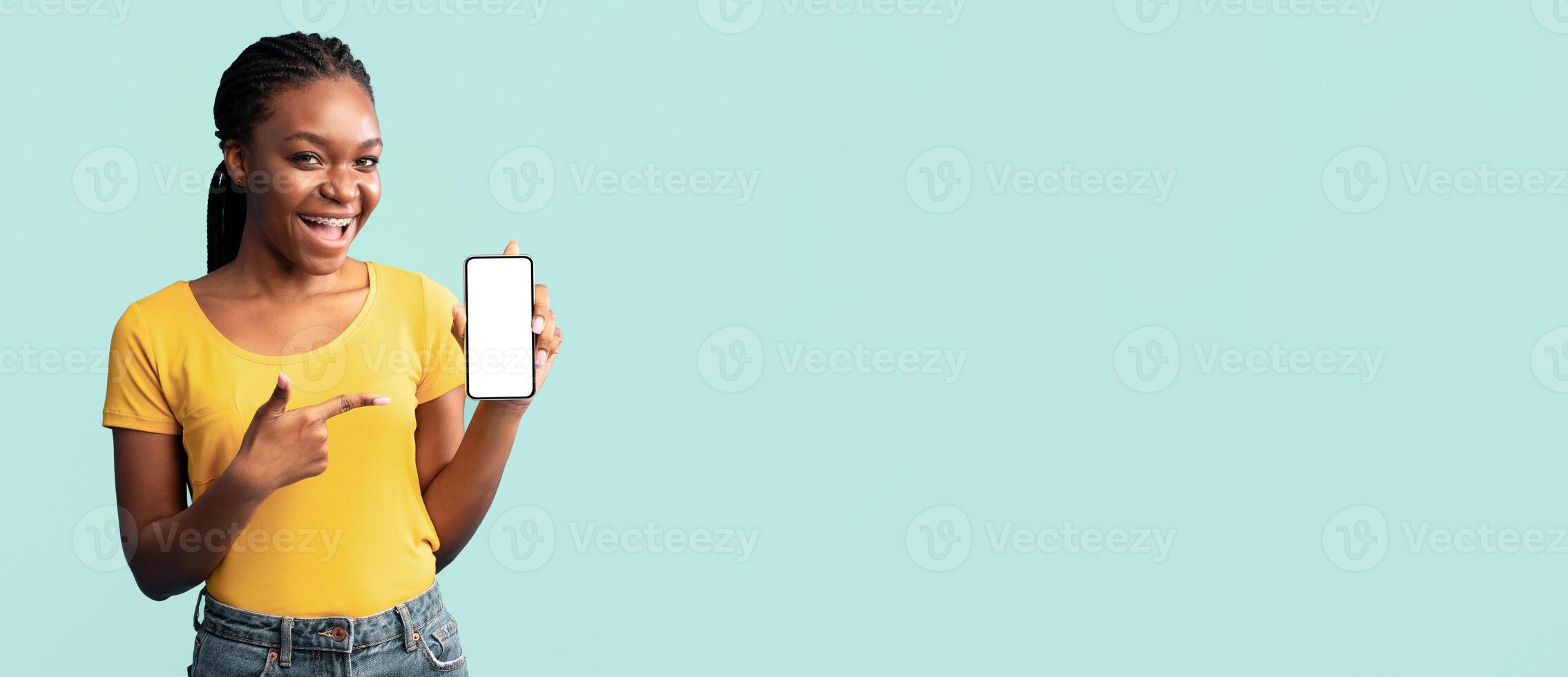 African Lady Showing Mobile Phone Empty Screen Posing Over Blue Studio Background. Cellphone Application. Mockup photo