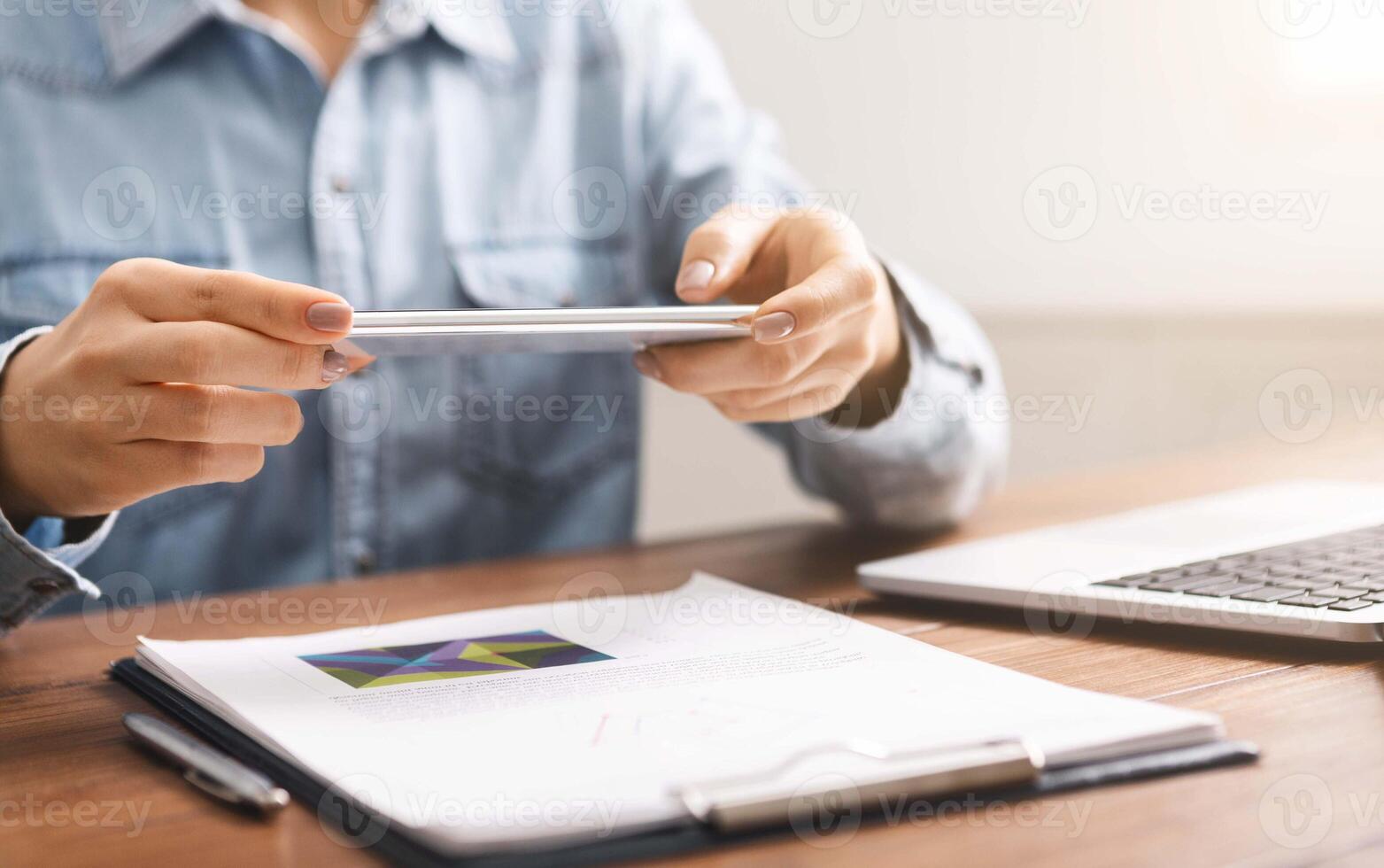 Woman holding smartphone in horizontal orientation taking photo of papers, using a scanner app for taking copies of the documents.