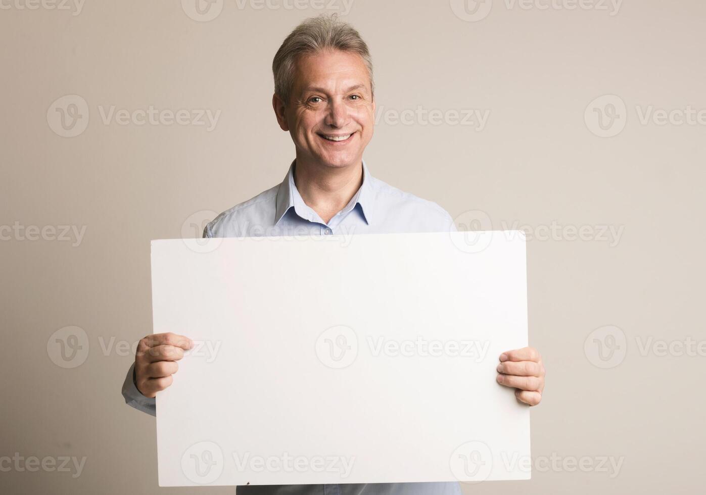 Happy mature man with blank advertising board over grey background, free space photo