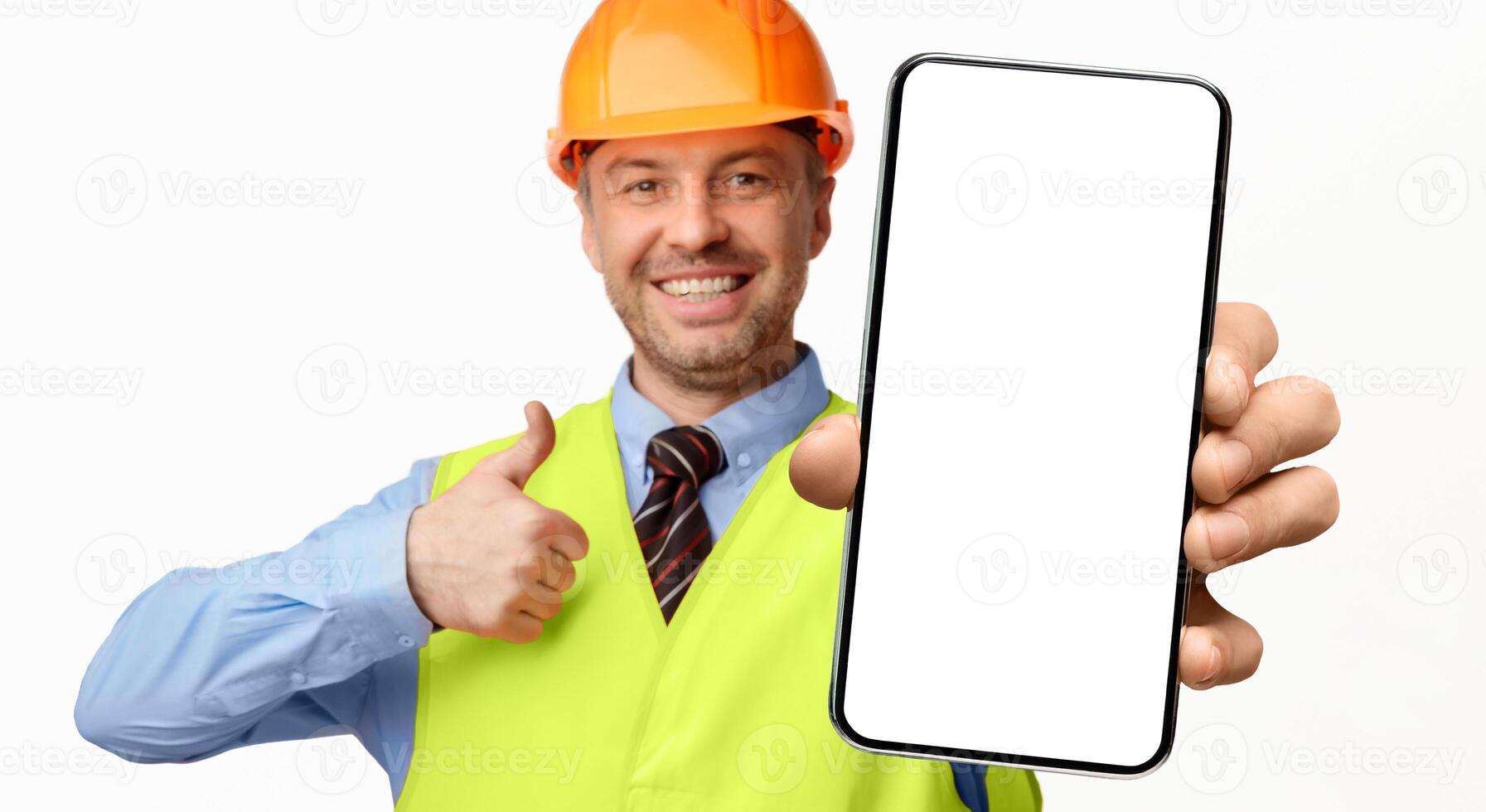 Construction Worker Showing Smartphone Empty Screen Gesturing Thumbs-Up, Recommending Architectural And Building Services On White Background. Selective Focus photo