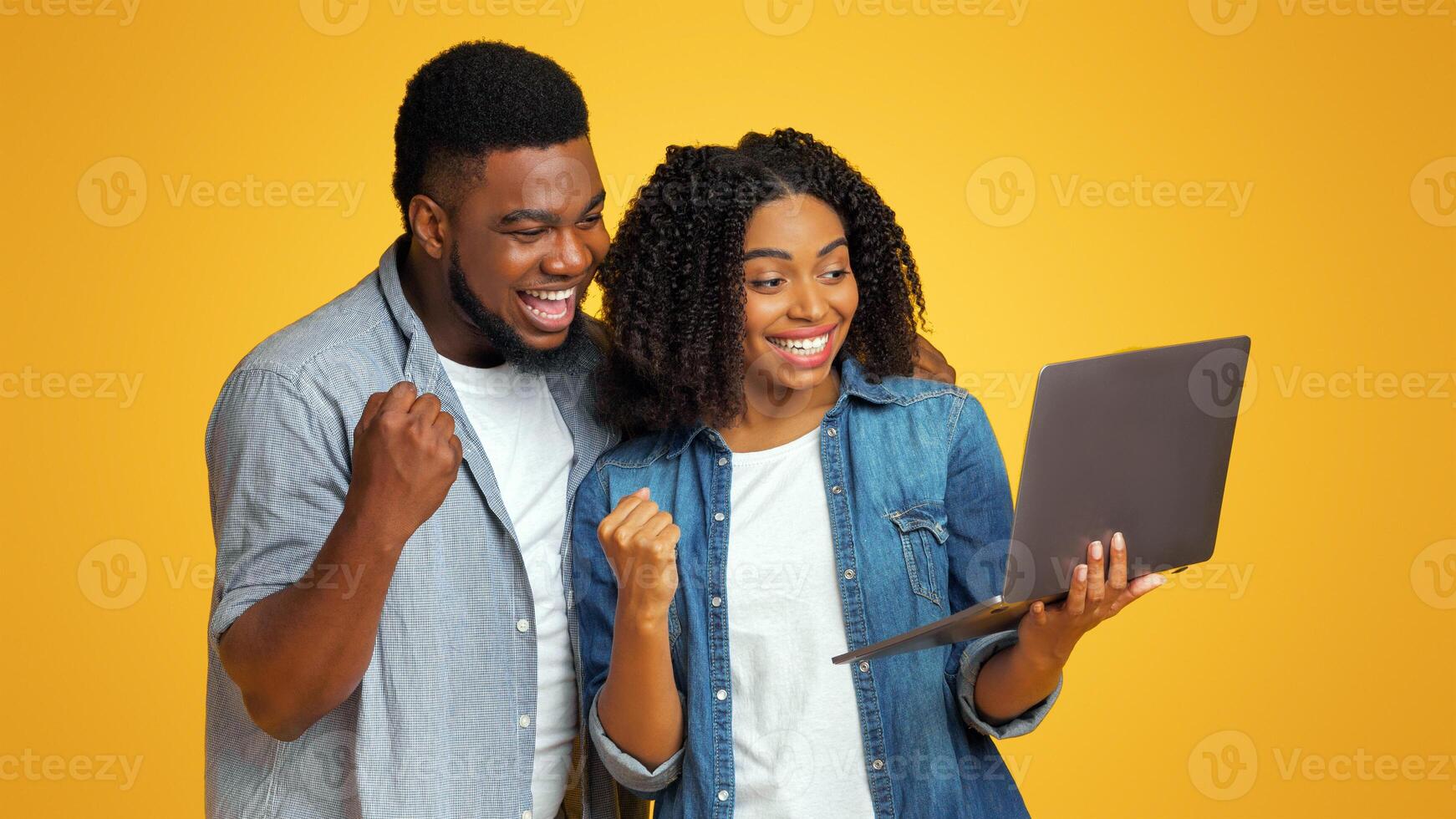 Smiling African American Couple Watching Sports On Laptop Together And Cheering, Standing Over Yellow Background With Copy Space photo