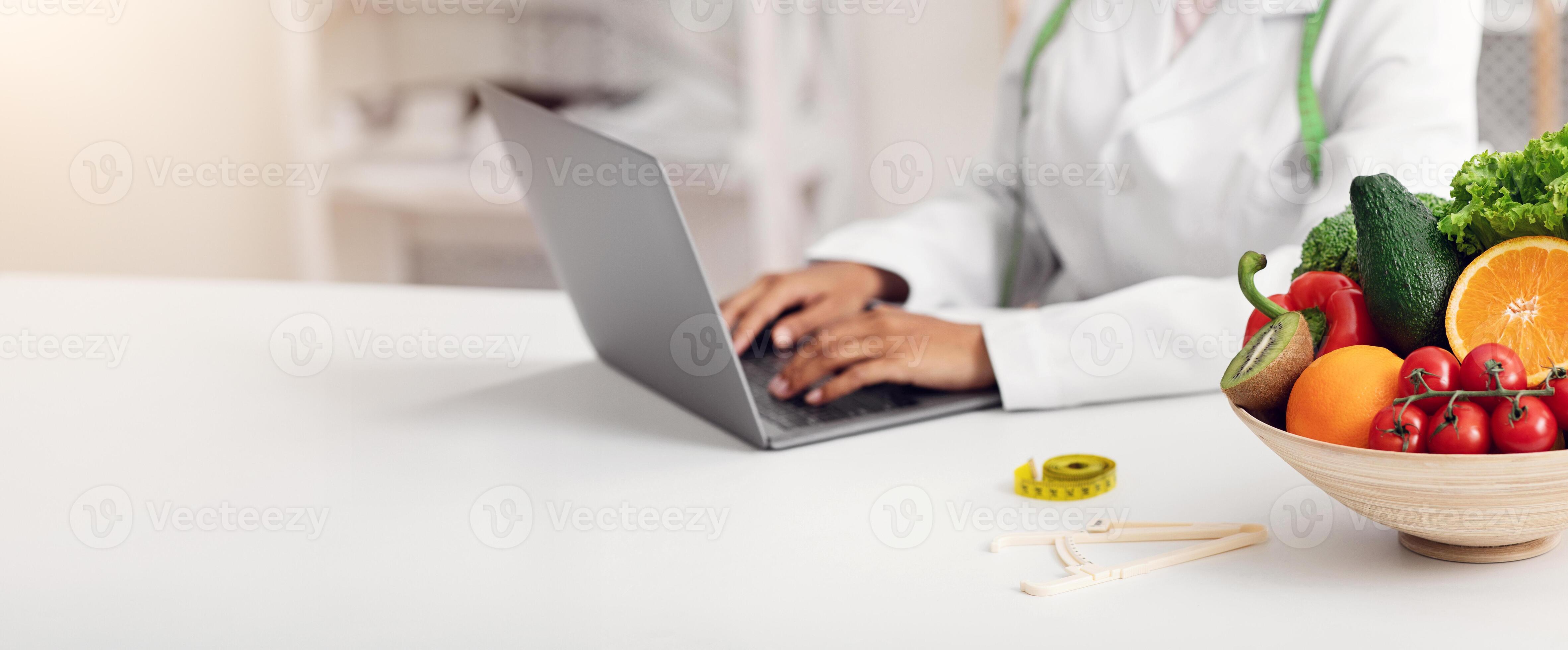 Cropped of black female nutritionist working with laptop at office Cropped of black female nutritionist working with laptop at office
