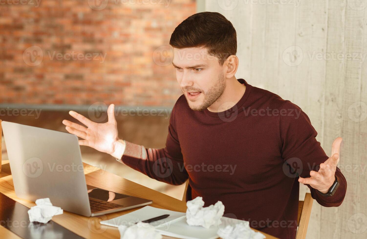 Angry Employee Guy At Laptop Gesturing With Hands Having Problem With Computer Sitting In Modern Office. Selective Focus photo