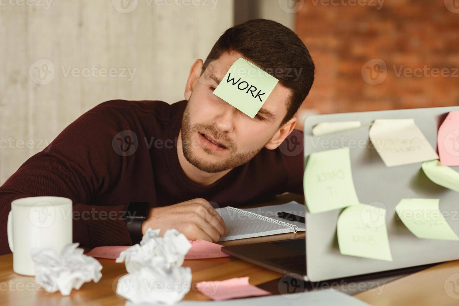 Overworked man having a nap sleeping at laptop with sticky notes everywhere, tired of office multitasking work indoor. Selective Focus photo