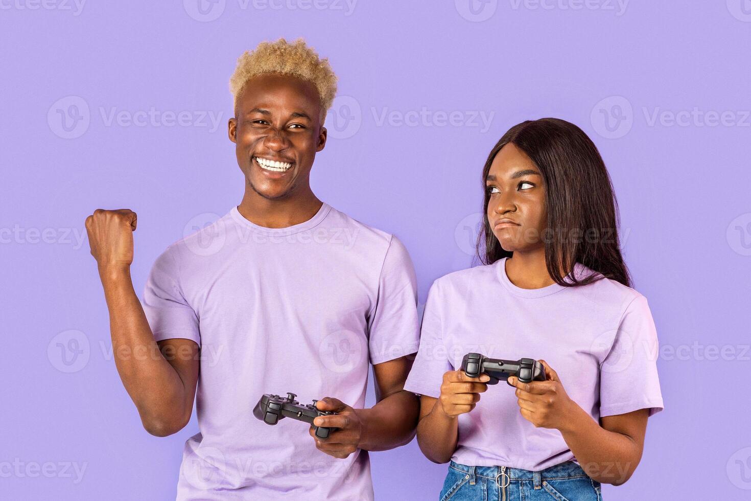 Happy African American guy and his upset girlfriend with game controllers on violet background photo