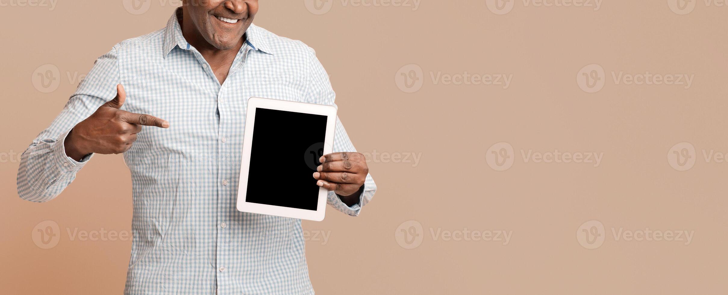 African american man showing big modern digital tablet with blank screen, orange background, empty space photo