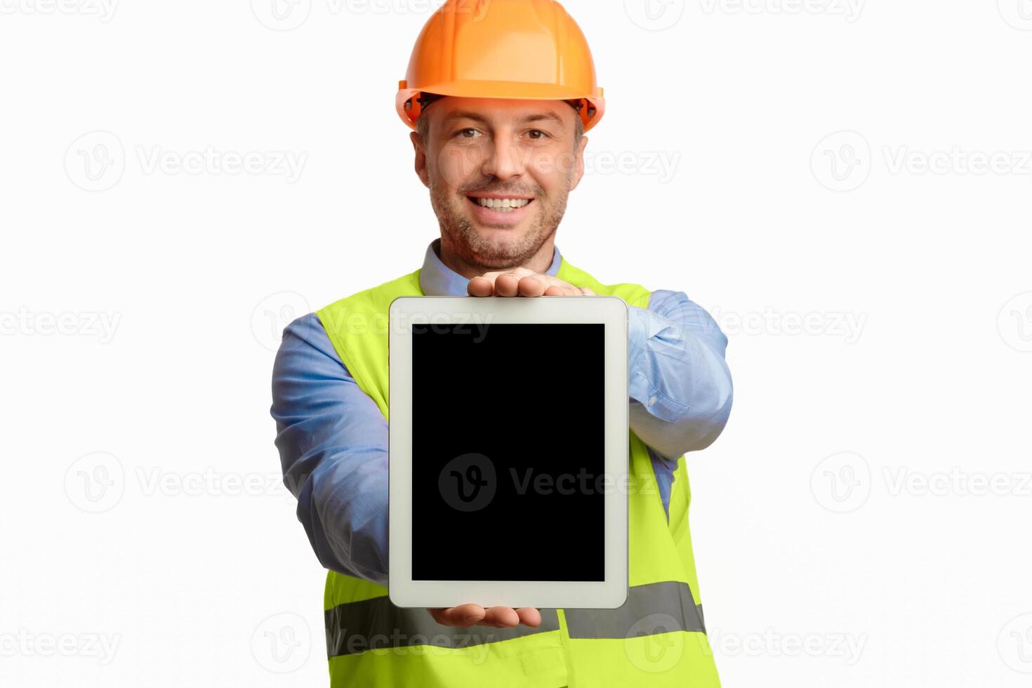 Repairman Showing Digital Tablet Empty Screen Standing Over White Studio Background, Wearing Vest And Helmet. Selective Focus, Mockup photo
