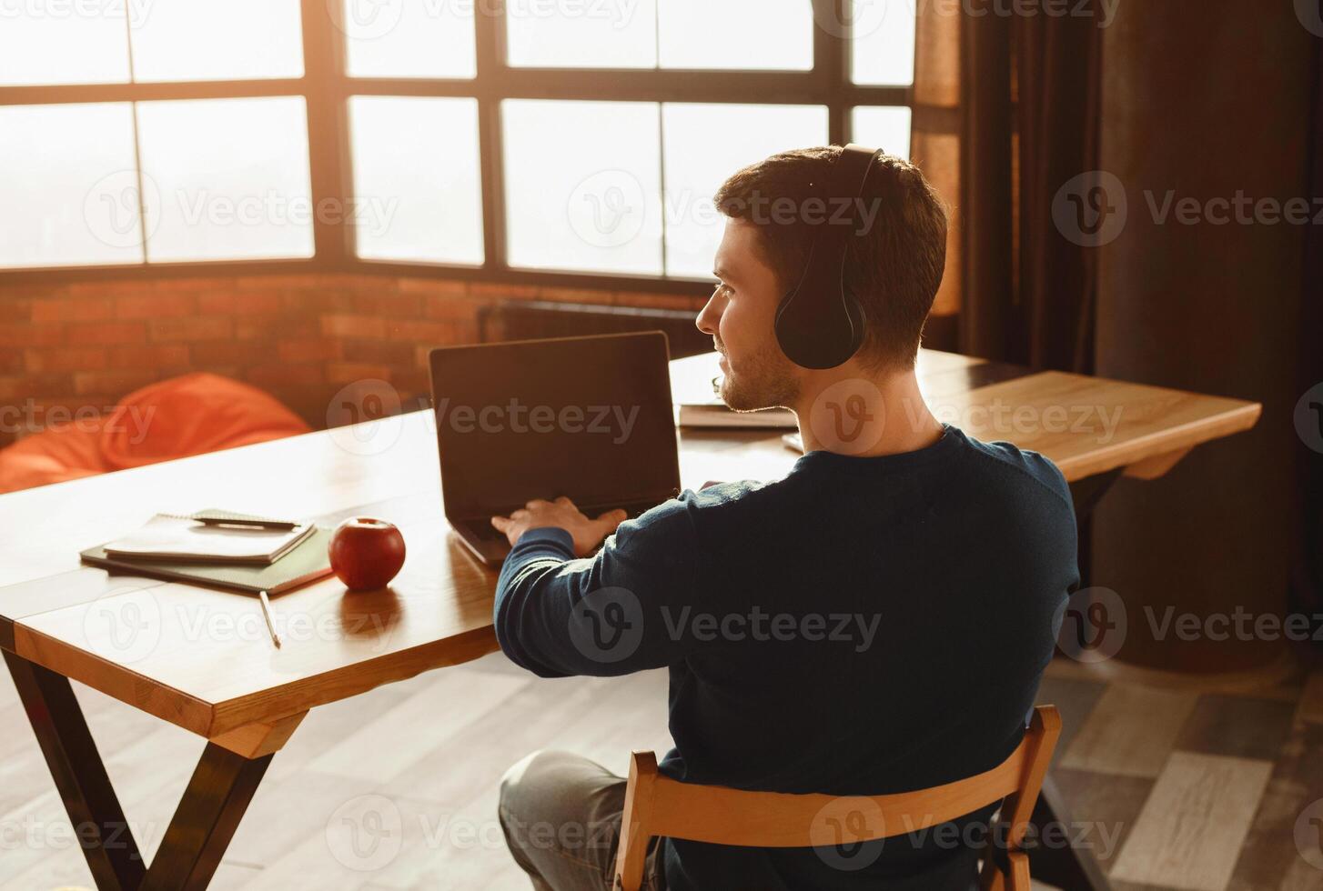 Unrecognizable Freelancer In Headphones Working On Laptop Computer Sitting In Coworking Workspace. Back View photo