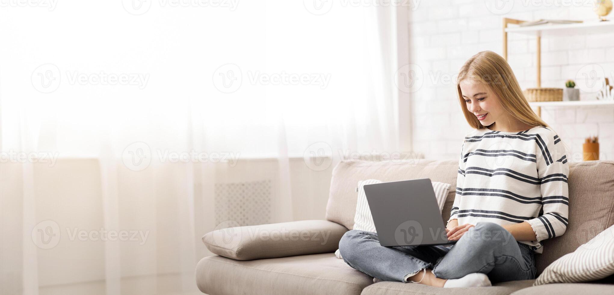 Looking for job. Student girl using laptop, sitting on couch, home interior, copy space photo