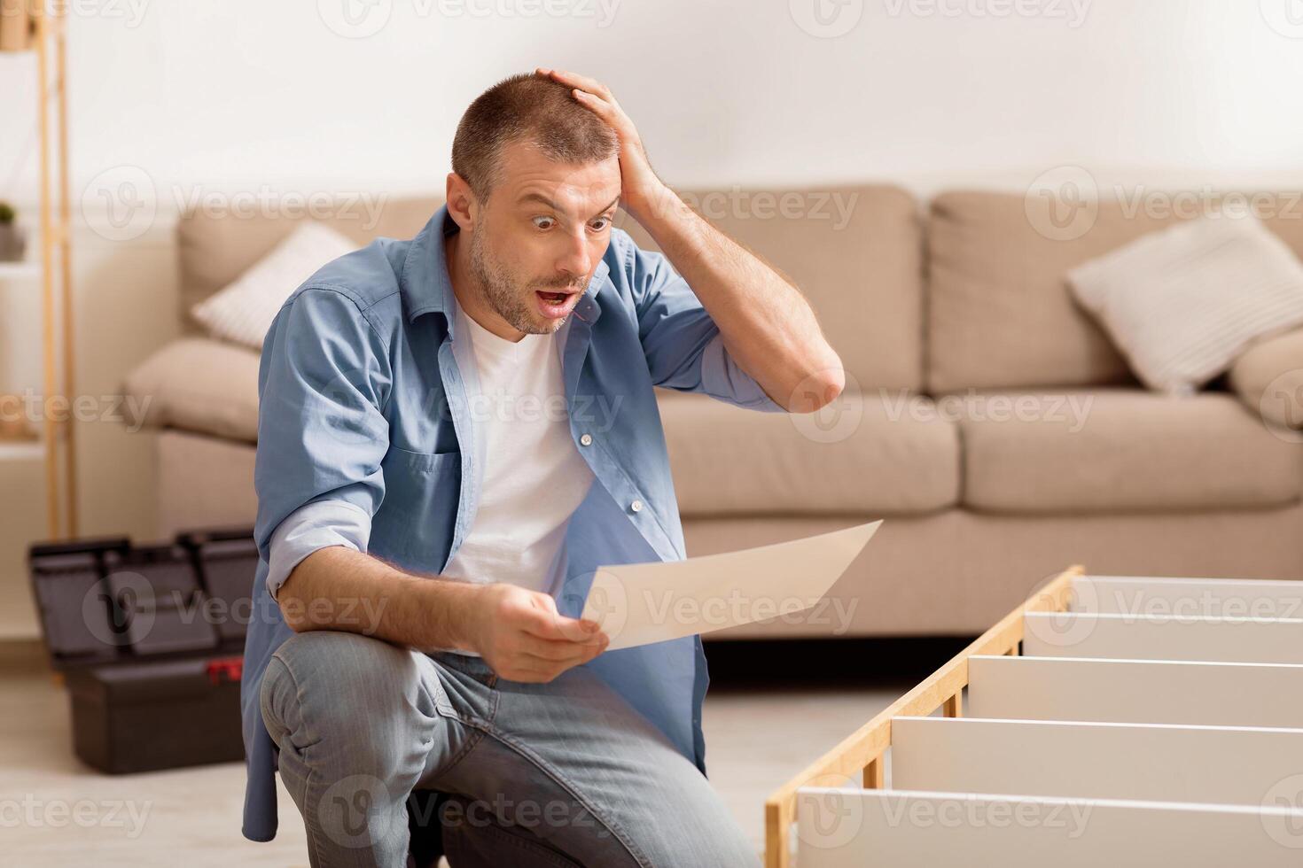 Self-Assembly Furniture. Shocked Man Looking At Shelf Installation Instruction Scratching Head Making Renovation At Home. Selective Focus photo
