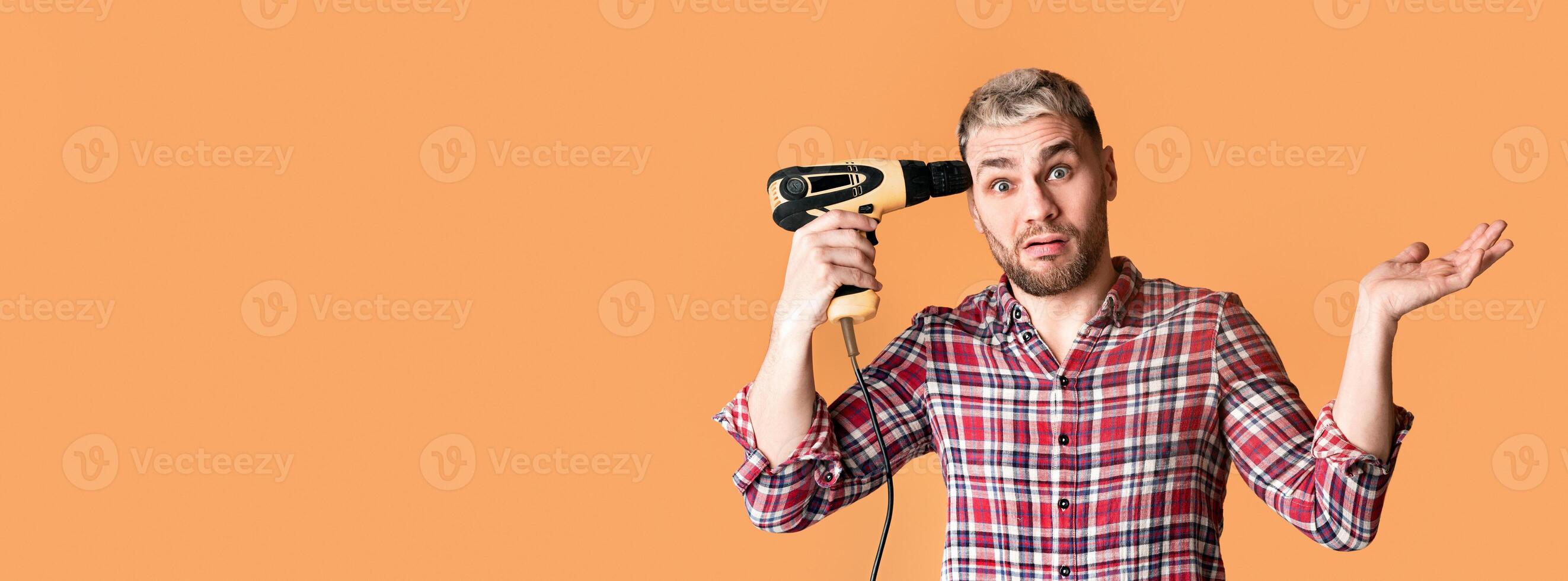 Emotional man sad due to repair, holding drill at temple on yellow background, empty space photo
