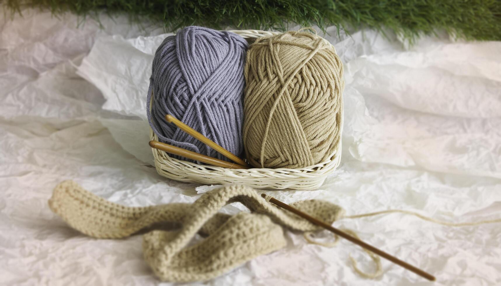 In selective focus of two Yarn balls in woven basket put at the back of blurred knitting work, photo