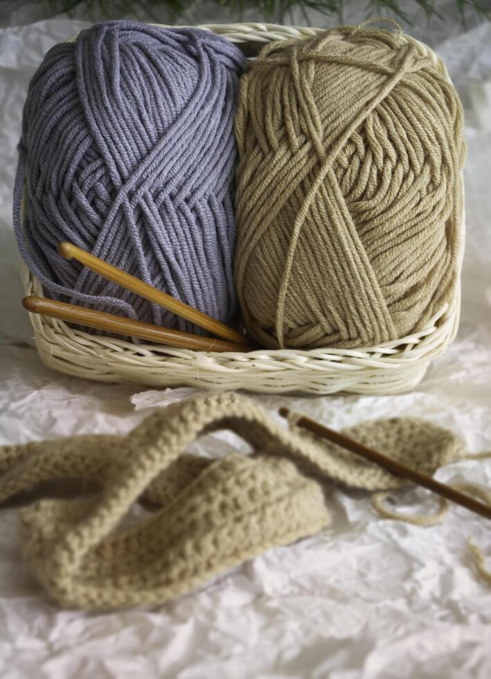 In selective focus of two Yarn balls in woven basket put at the back of blurred knitting work, photo
