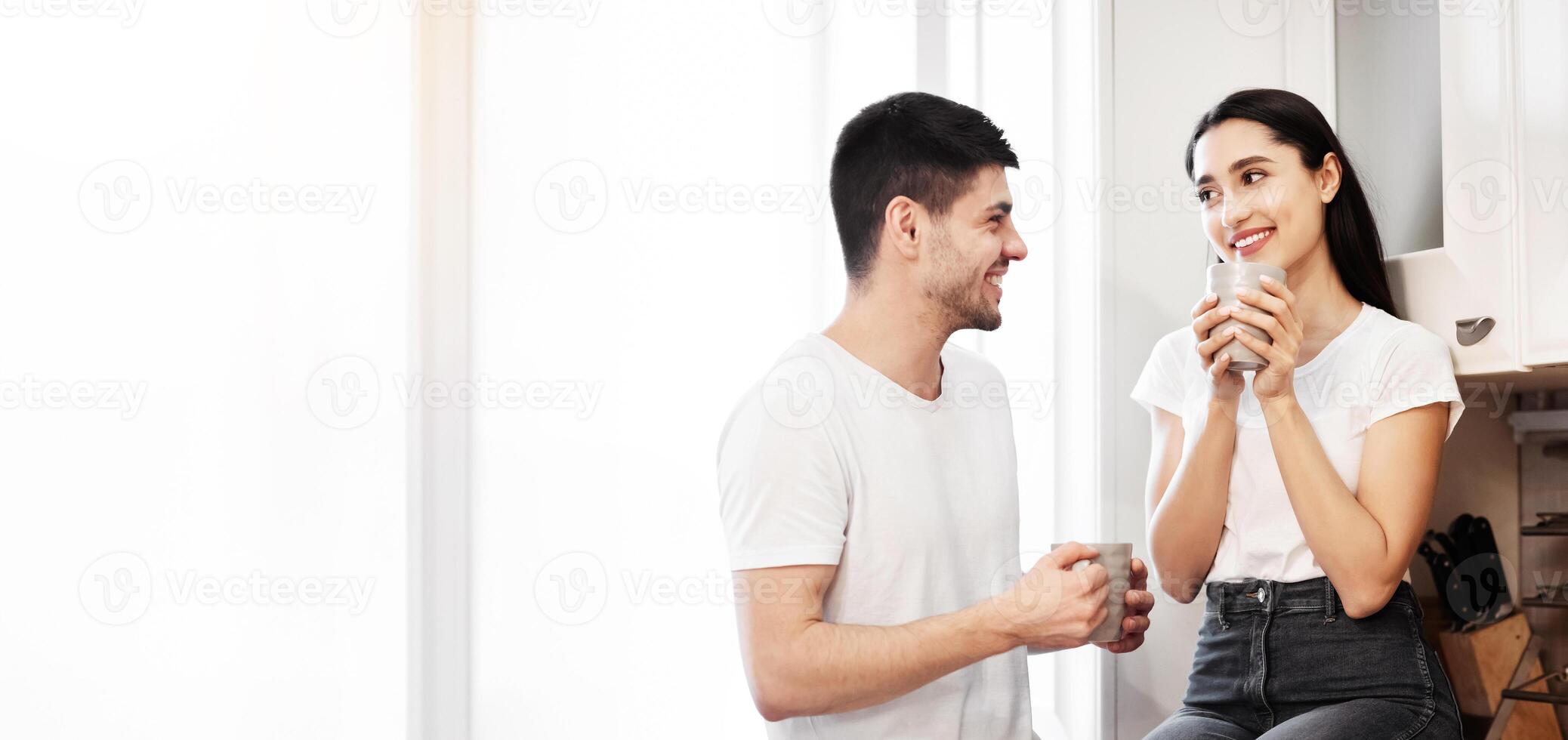 Lovely Family Concept. Portrait of cheerful couple drinking tea in modern kitchen in the morning, looking at each other photo