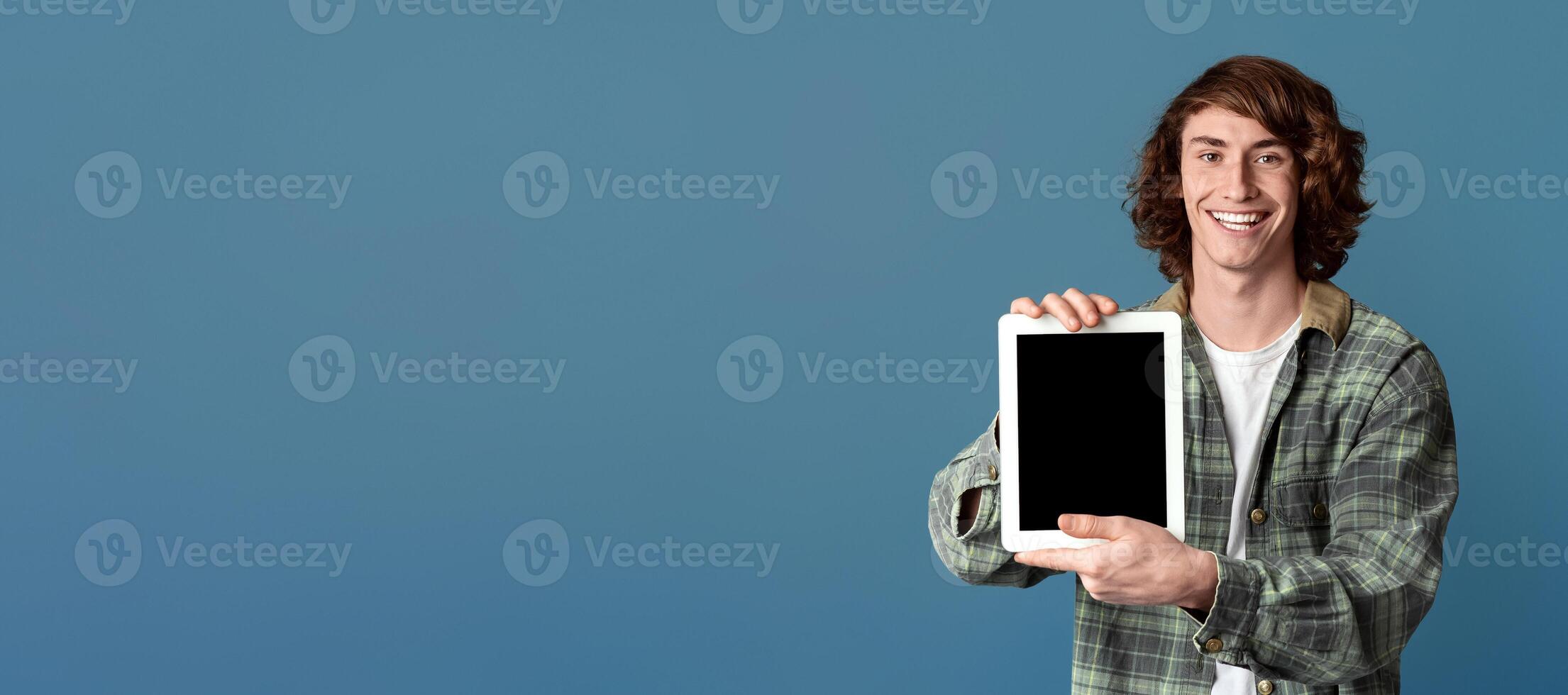 Smiling teenage guy showing tablet computer with empty screen on turquoise background, space for design photo