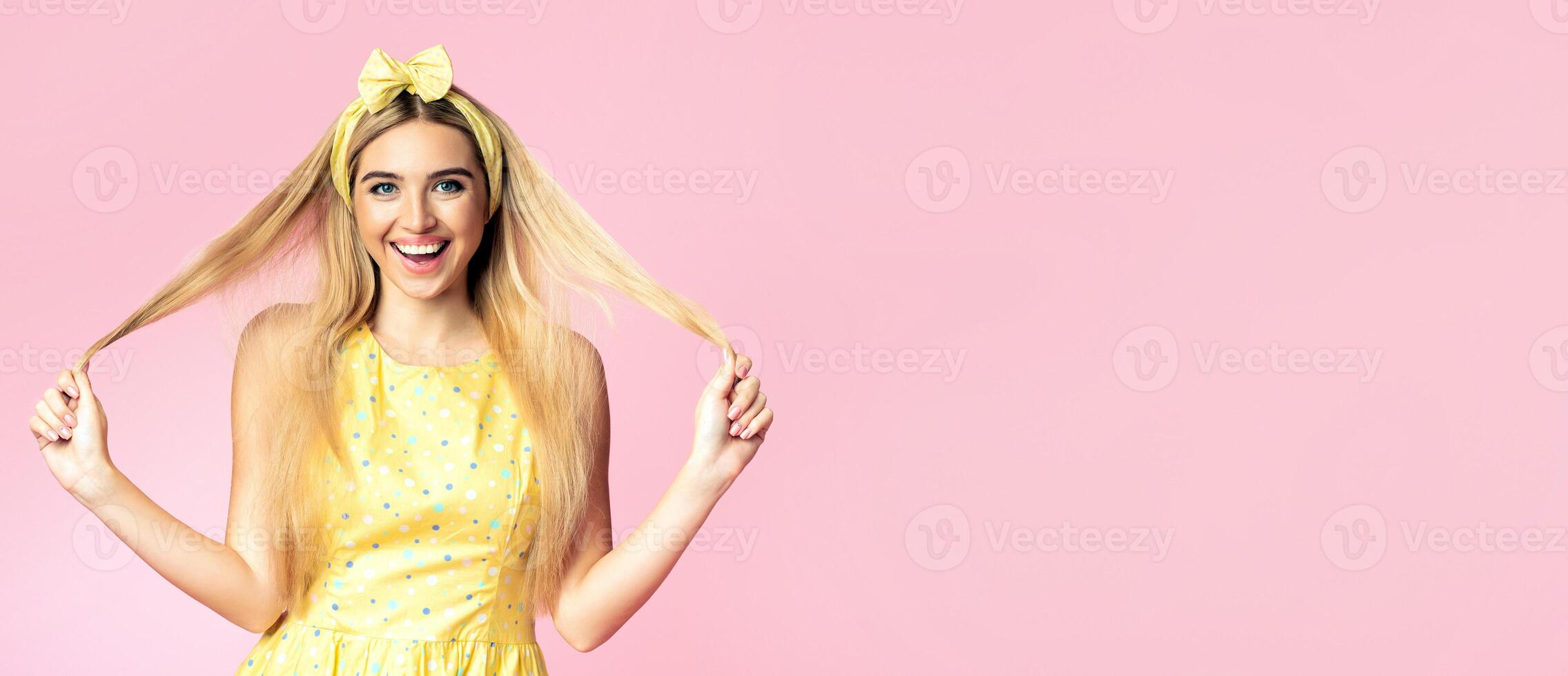 Enjoying Life. Smiling blonde girl playing and touching her long beautiful hair over pink studio wall, copyspace photo