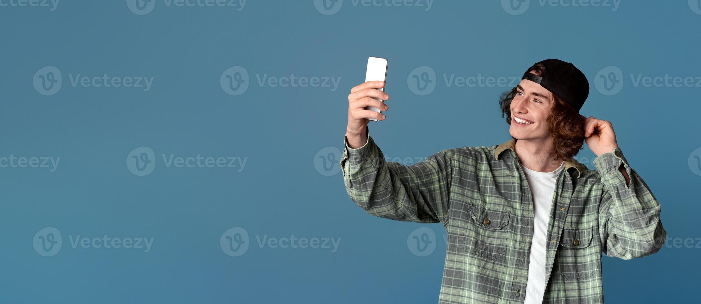 Happy young hipster taking selfie with smartphone against turquoise background photo
