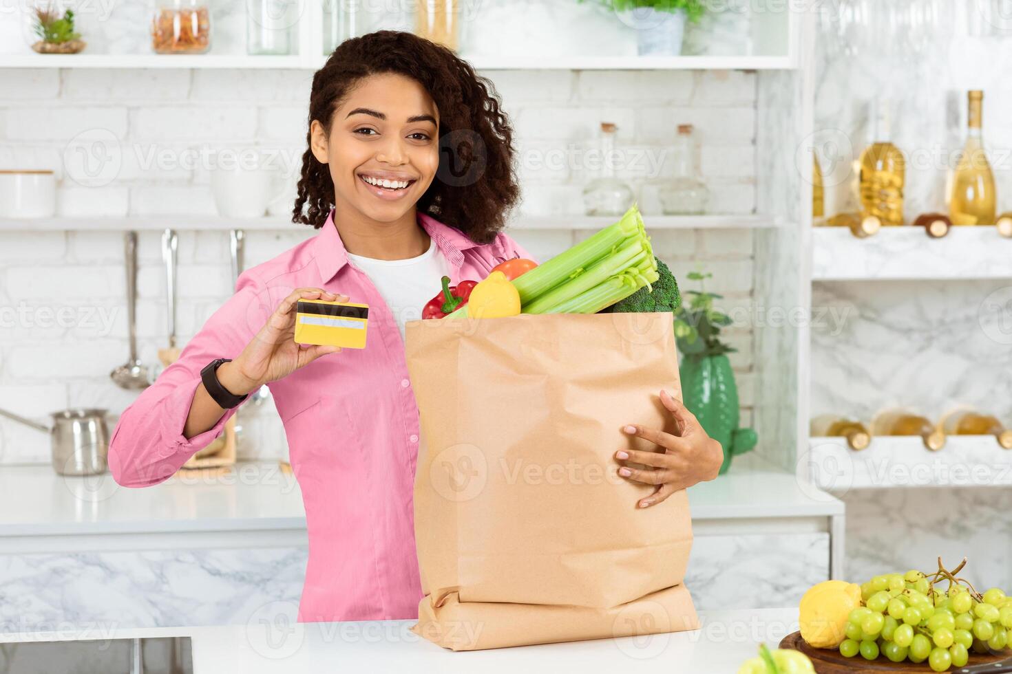 Food Delivery Service. Smiling black woman holding credit card and paper bag with food, standing in kitchen, free space photo