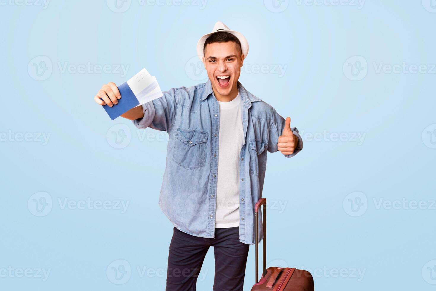 Emotional young man tourist with luggage holding passport and tickets, orange background photo