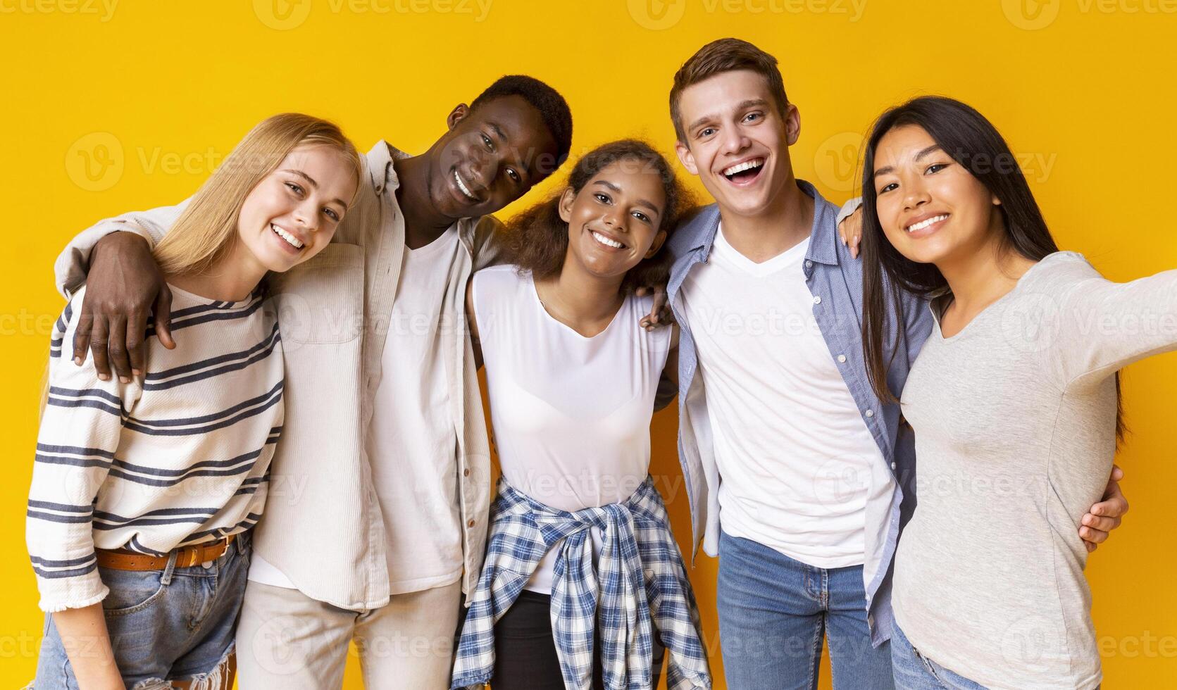Friendly international group of teenagers embracing and taking selfie over yellow background photo