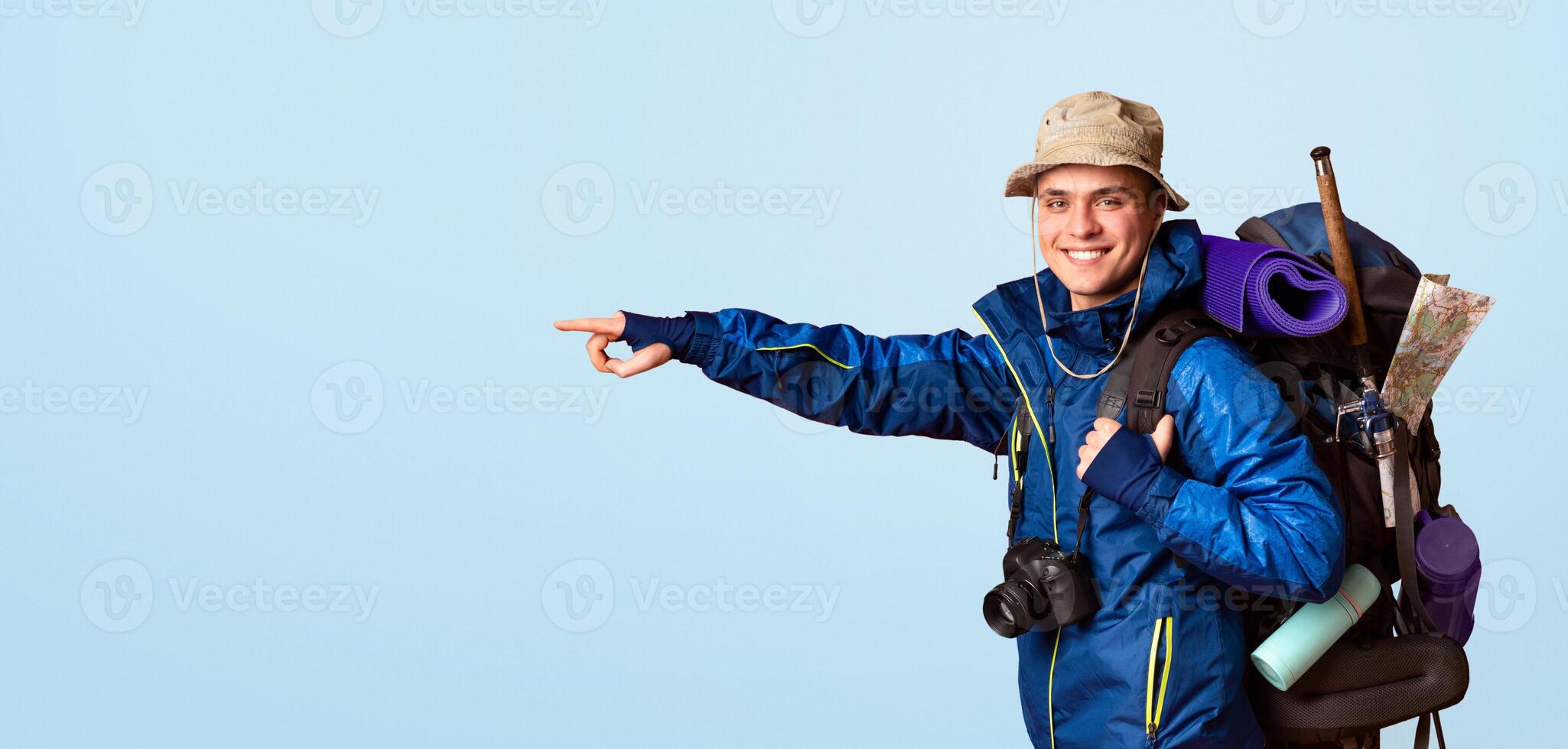 Hiking equipment shop advertising. Excited young man backpacker pointing at copy space, orange background, panorama photo