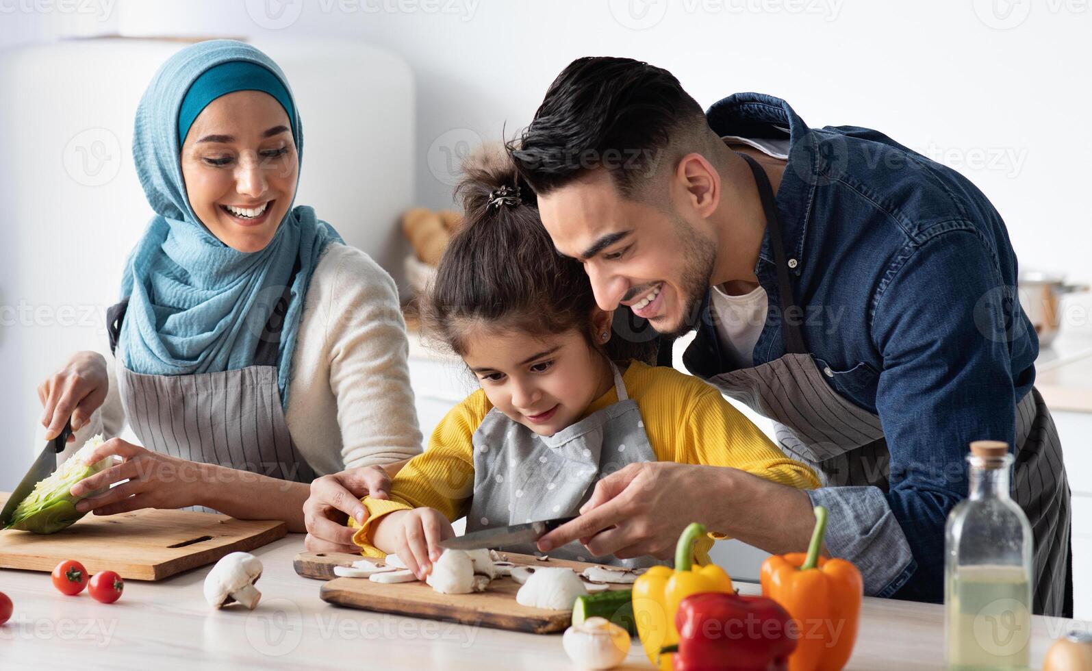 Young Arab Father Showing How To Chop Mushrooms To His Little Daughter While They Cooking Healthy Tasty Food Together At Home, Happy Muslim Family Of Three Enjoying Preparing Vegetarian Meal photo