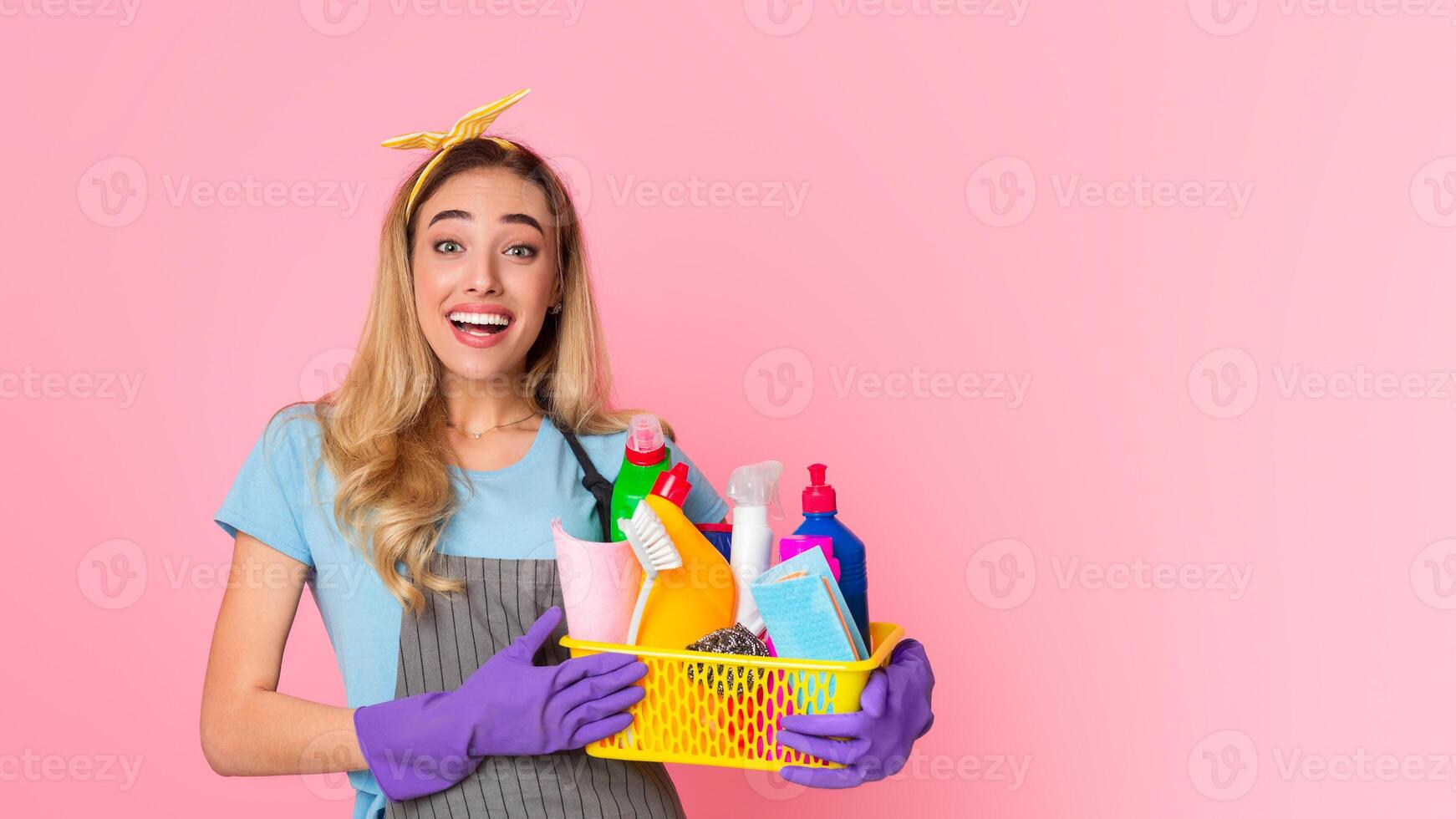 Start of house cleaning. Happy housewife with basket with cleaning supplies isolated on pink background, studio shot photo