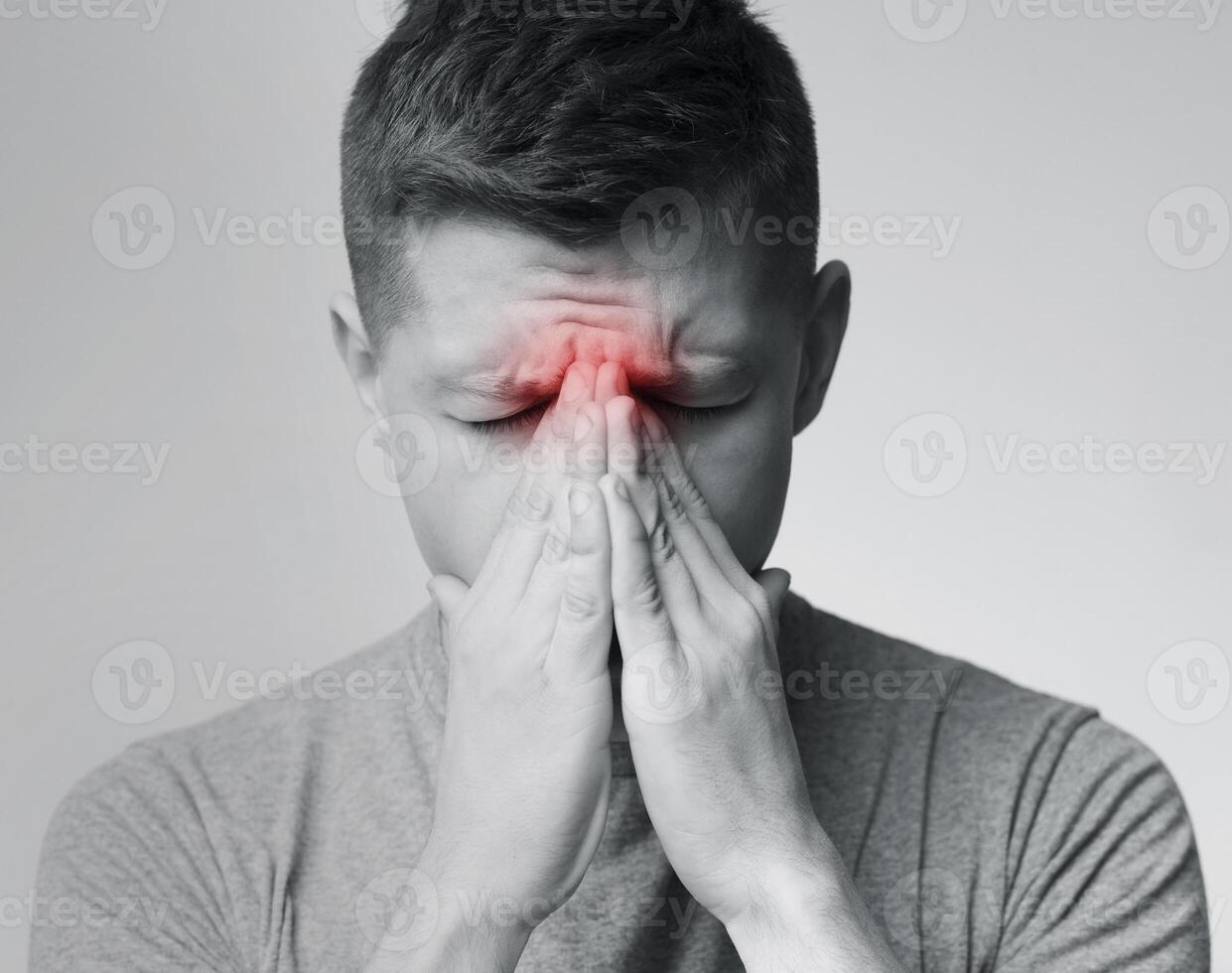 Sinus pain, sinusitis. Sad man holding his nose, black and white photo with red sore zone