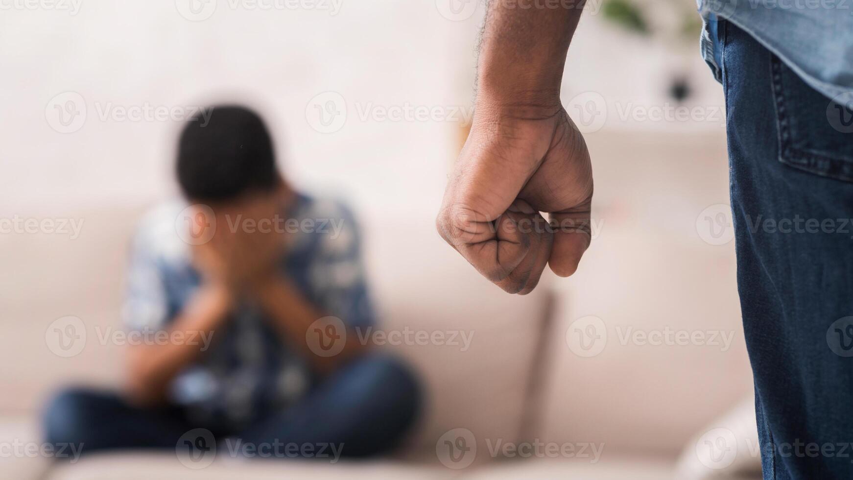 Domestic violence. Scared black little boy suffering from home abusement, afraiding of father's fist, sitting on sofa and crying, selective focus photo