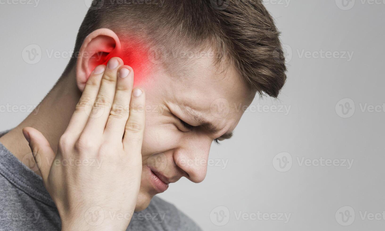 Young man has sore ear, suffering from otitis, touching his inflamed head, close up, empty space photo